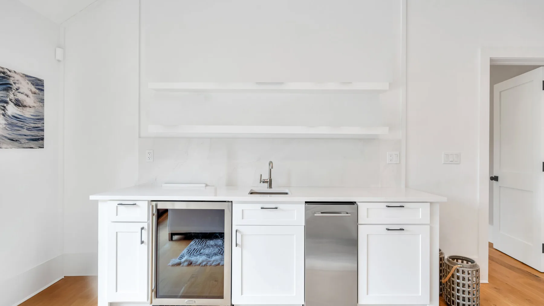 Una pequeña cocina luminosa con gabinetes blancos, un fregadero y un lavavajillas de acero inoxidable.