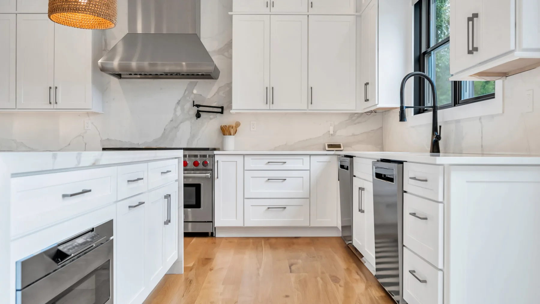 Una cocina luminosa con gabinetes blancos, electrodomésticos de acero inoxidable y piso de madera.