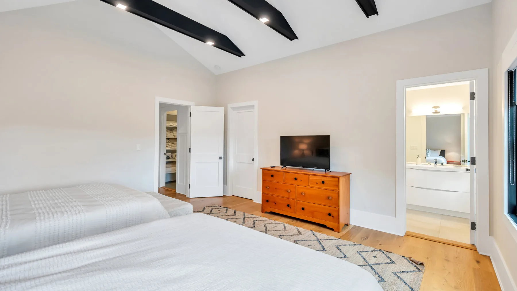 Un dormitorio luminoso con dos camas, una cómoda y un televisor.
