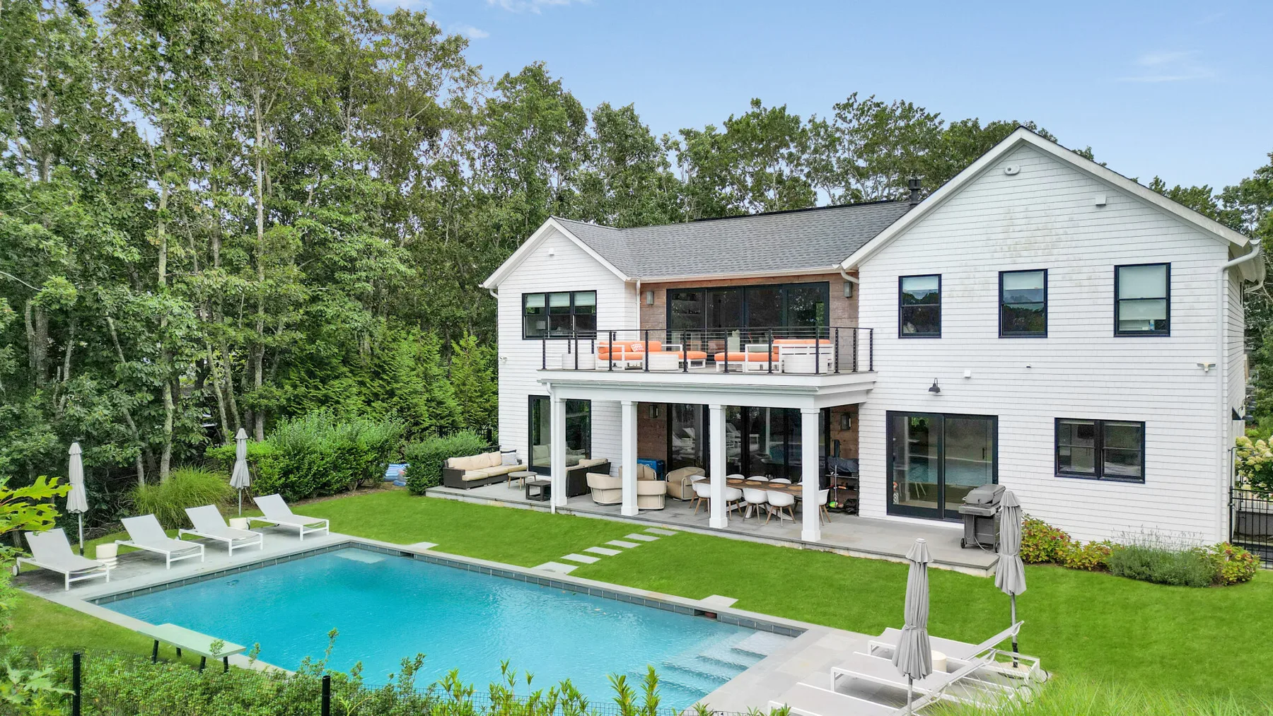 Una casa blanca da a una piscina al aire libre y un césped.