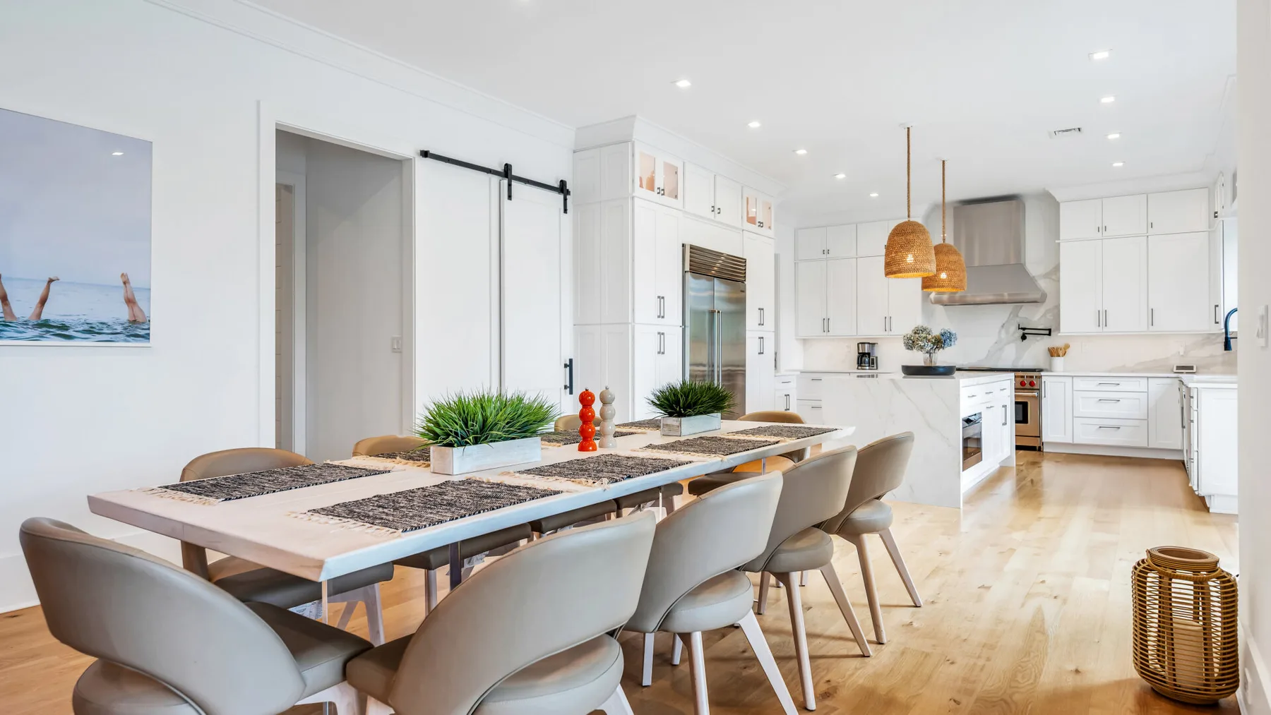 Un comedor luminoso junto a una cocina blanca, con una mesa larga y asientos tapizados.