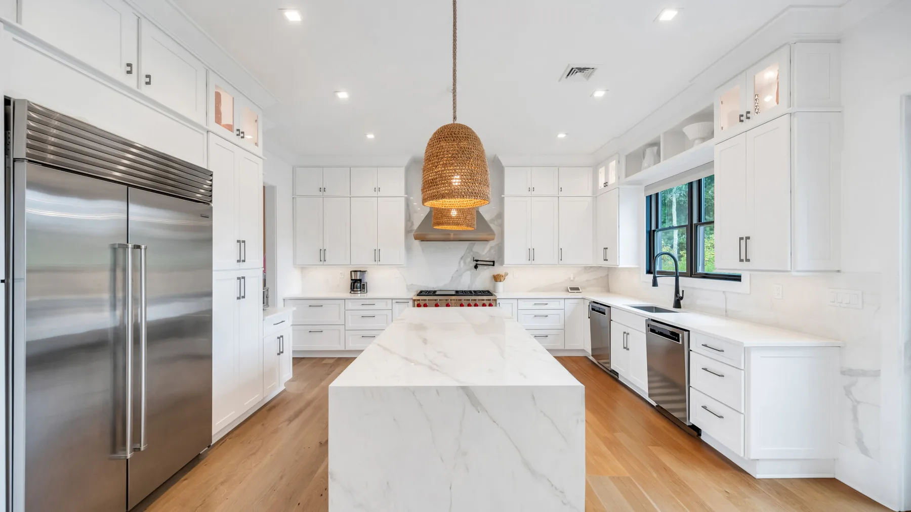 Una cocina blanca y luminosa con una isla grande y electrodomésticos de acero inoxidable.