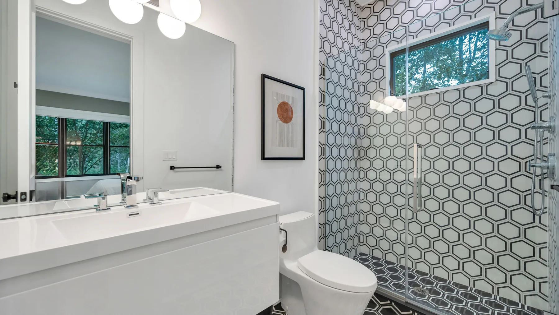 Un baño luminoso tiene un tocador largo junto a una zona de ducha con azulejos estampados.