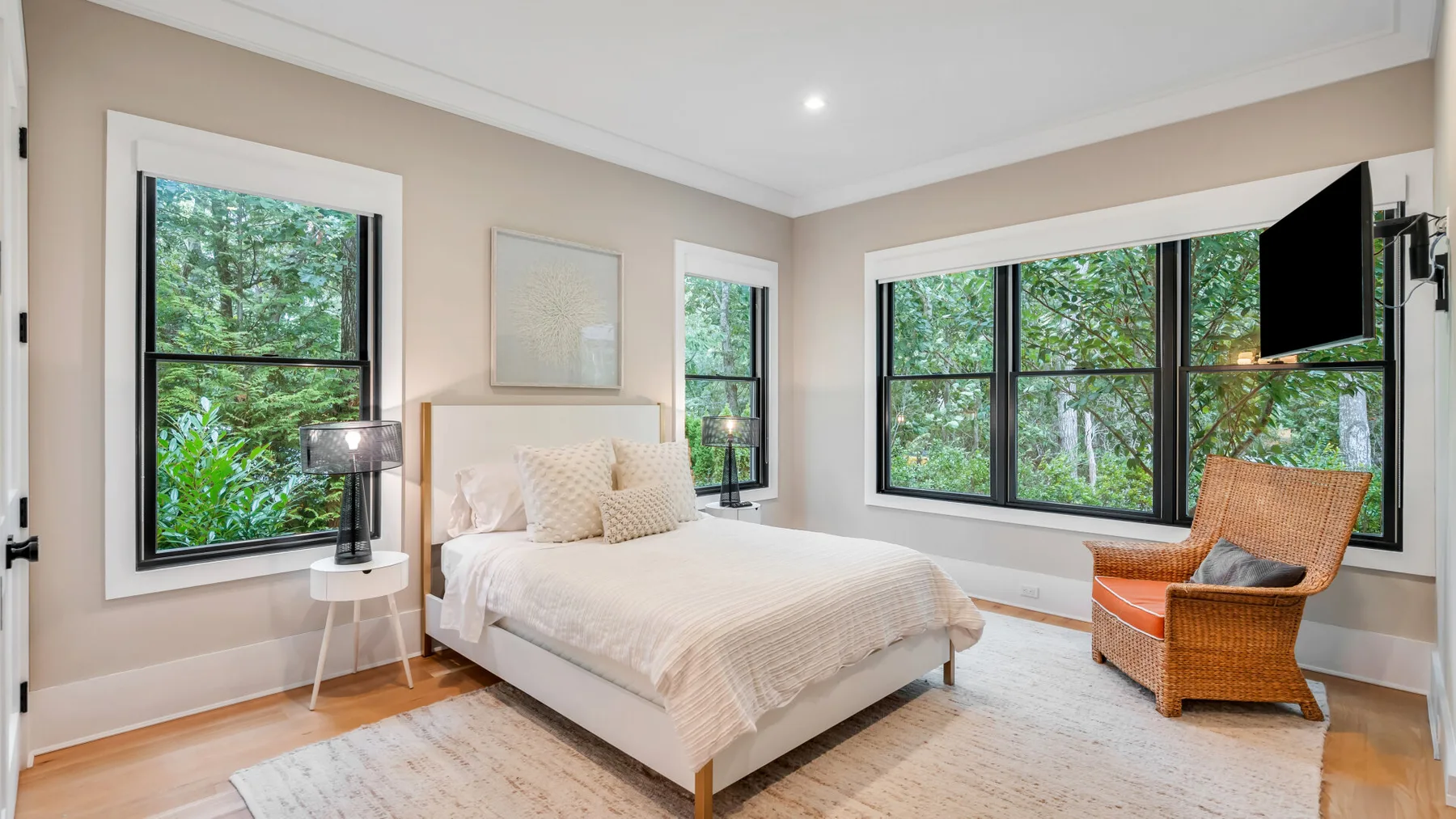 Un dormitorio luminoso con una cama, grandes ventanas y una silla tejida.