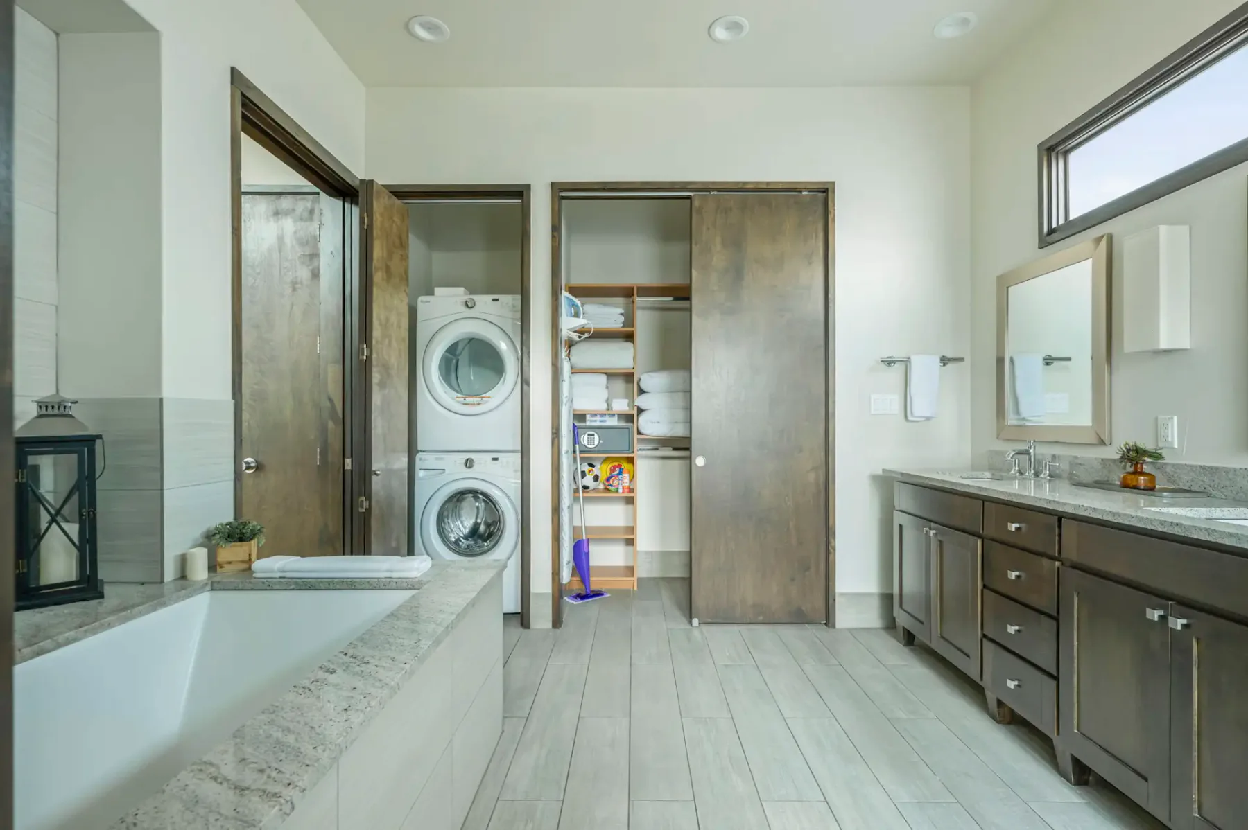 A spacious bathroom has a bathtub, double sinks, and stacked laundry appliances.