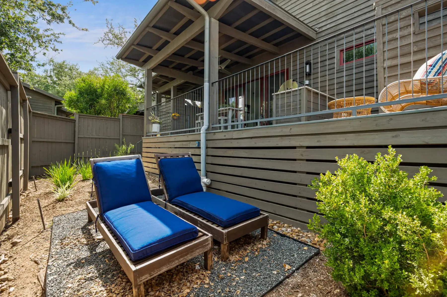 Two blue-cushioned lounge chairs on a patio, with a wooden deck above.
