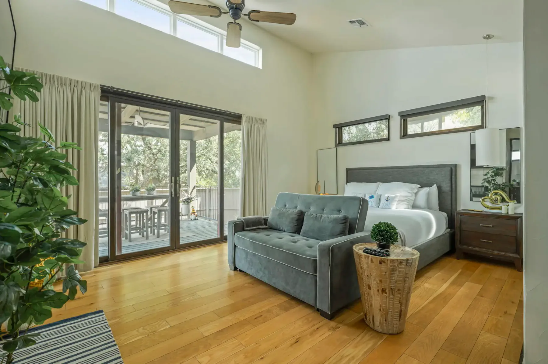 A bedroom with a large bed, gray seating, and glass doors opening to a balcony.