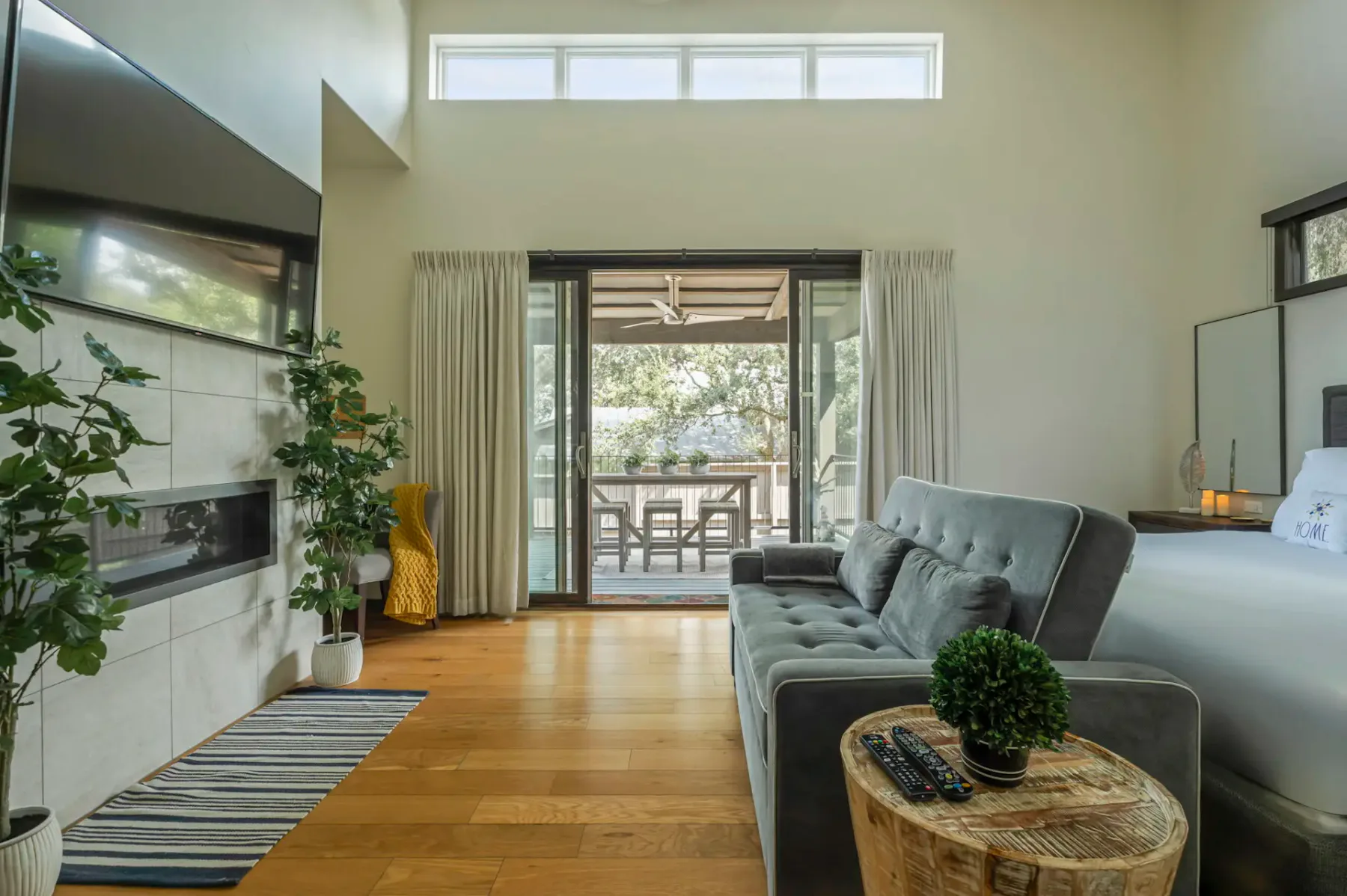 A bright living room with seating facing a wall-mounted television and an open sliding glass door.