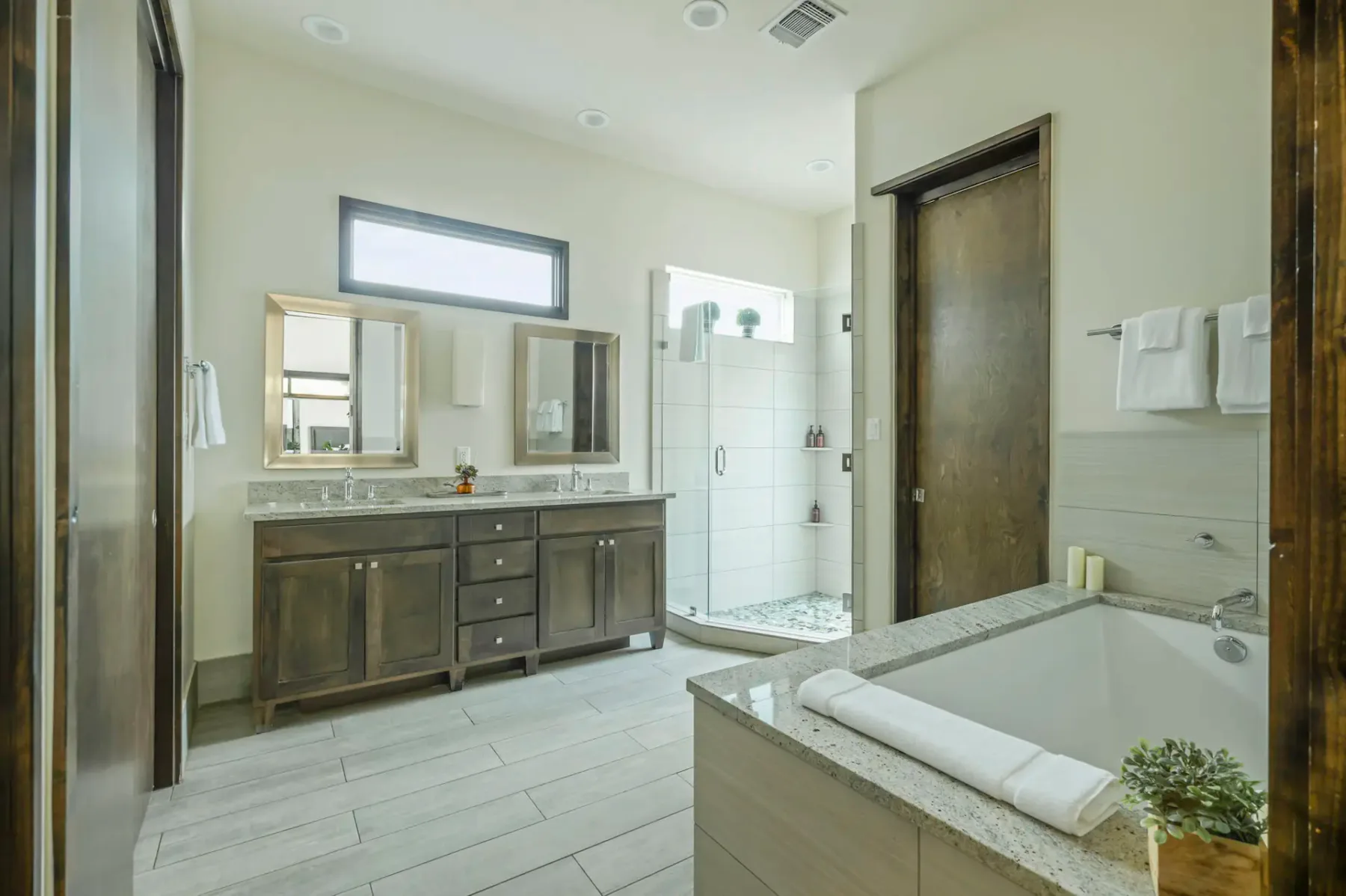 Modern bathroom with dual-sink vanity, large mirror, walk-in shower, and bathtub. Neutral tones and natural light enhance the spacious feel.
