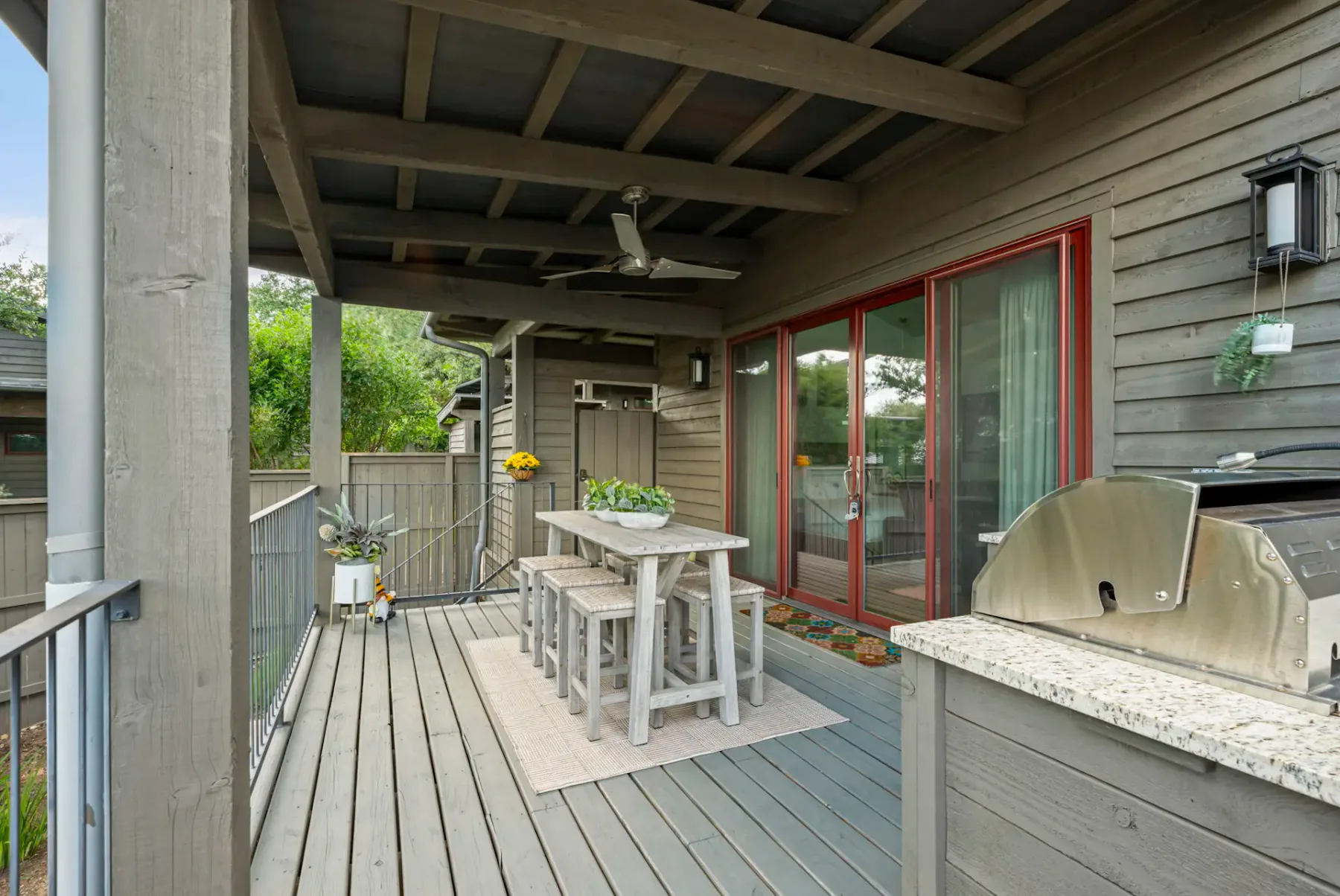 A covered wooden deck has a dining table beside red-trimmed sliding glass doors.