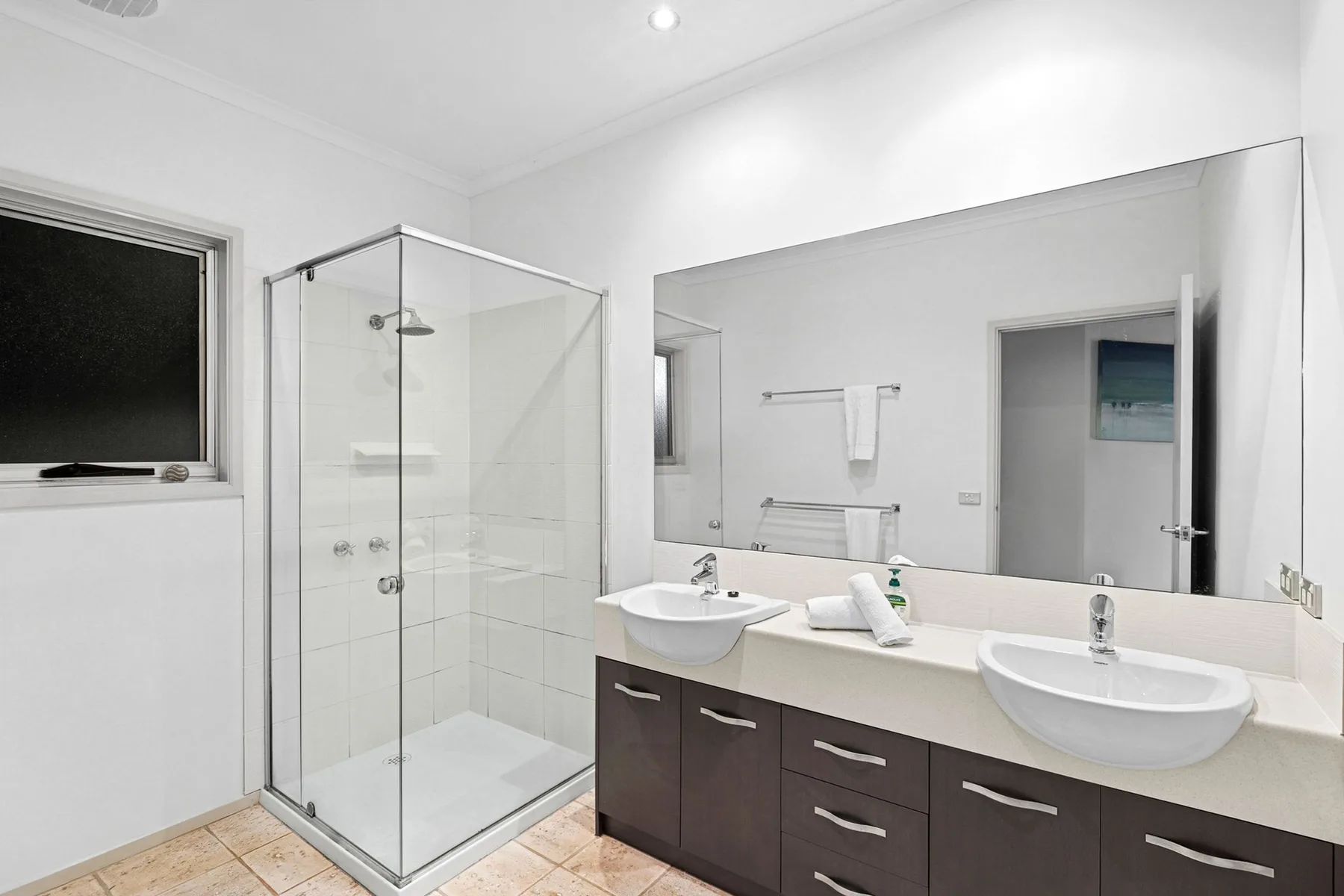 A bright bathroom with a glass shower, double sinks, and a long vanity.