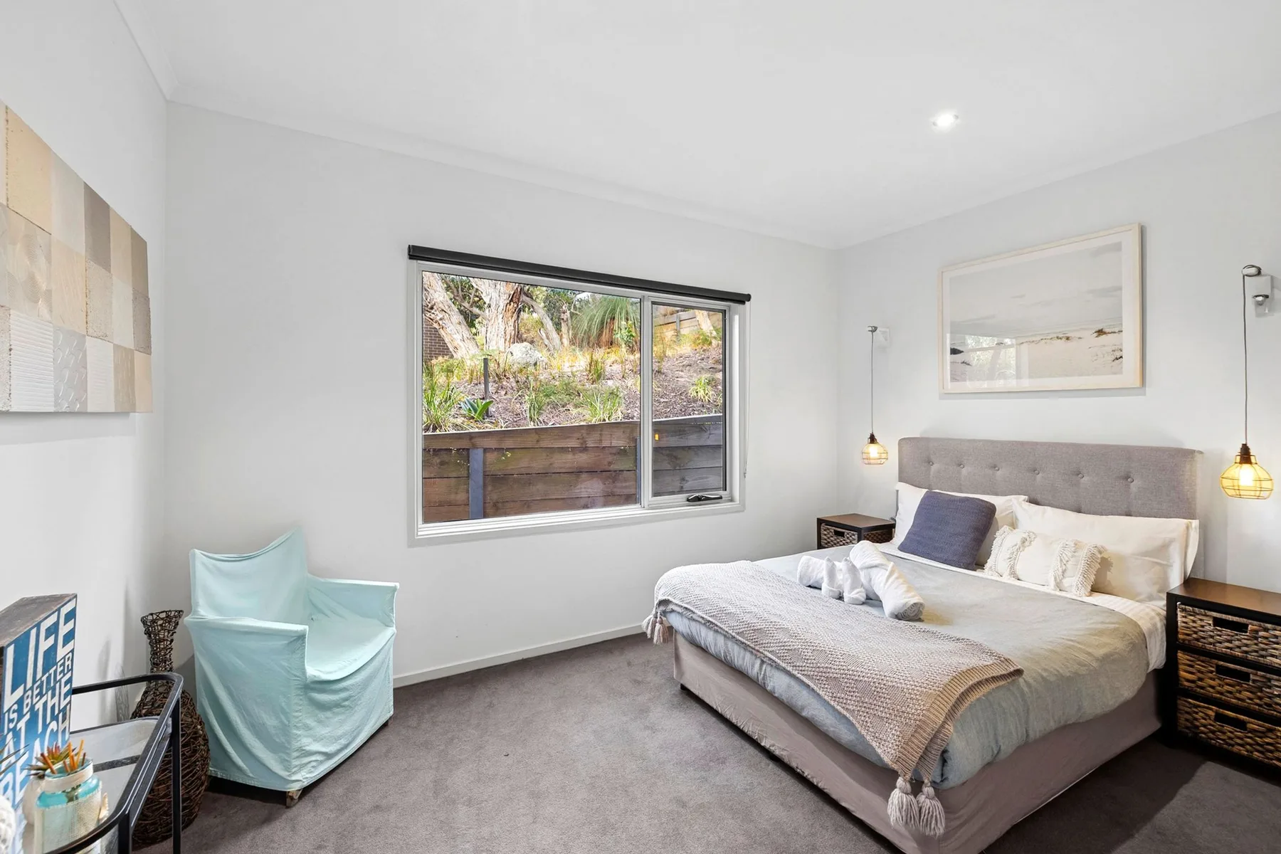 A bright bedroom with a bed, a window, and a small seating area.