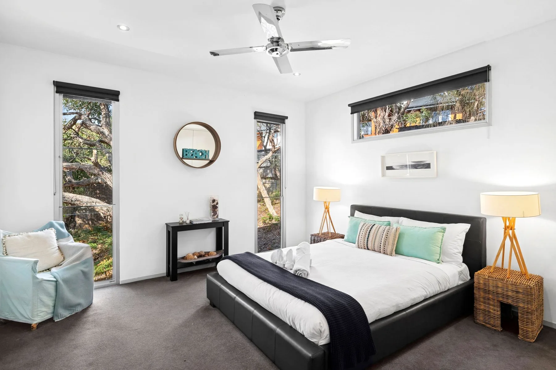 A bright bedroom with a large bed, bedside lamps, and tall windows.
