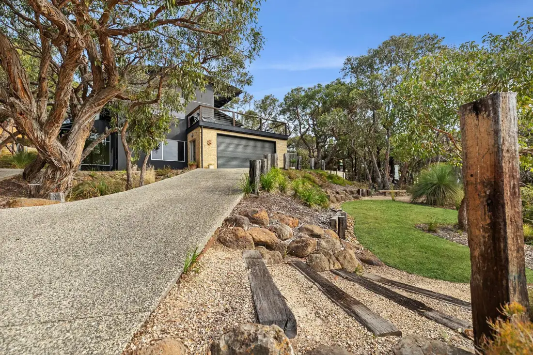 A modern house sits beside a sloped driveway and landscaped garden.