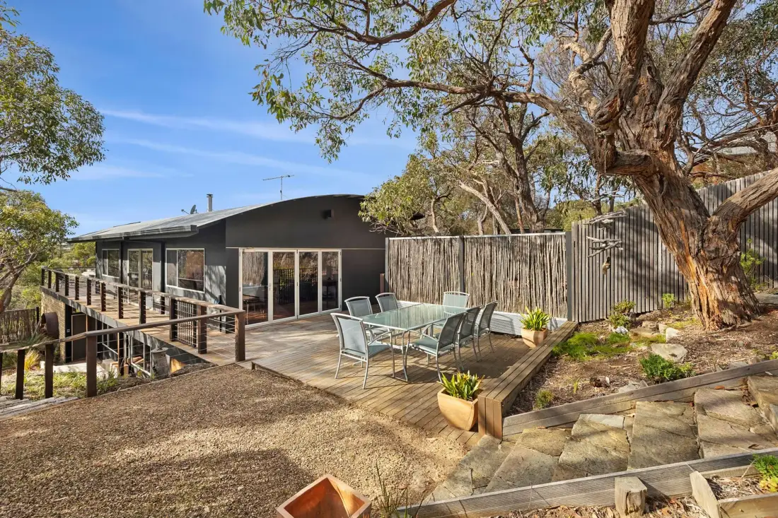 Modern house with a wooden deck, outdoor seating, and surrounding trees.