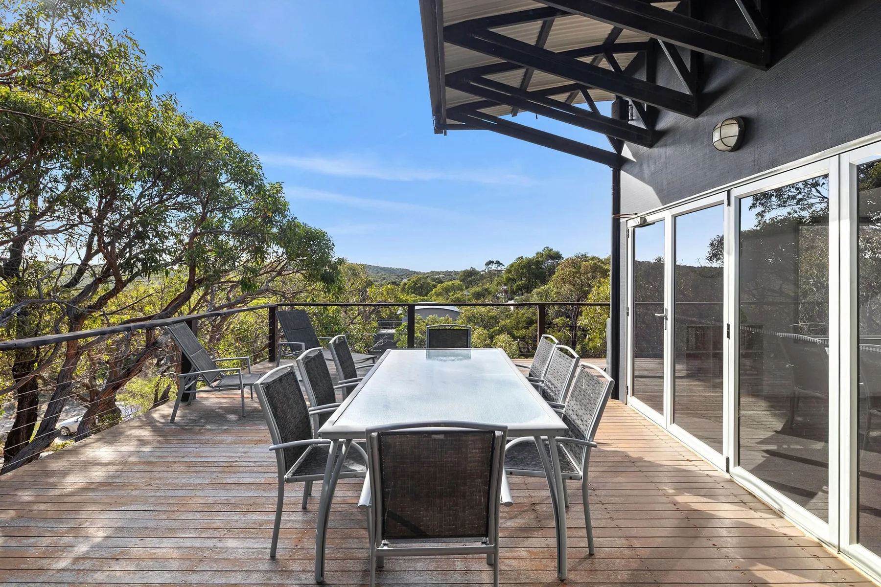 An outdoor dining area with a table and seating overlooks a tree-lined landscape.