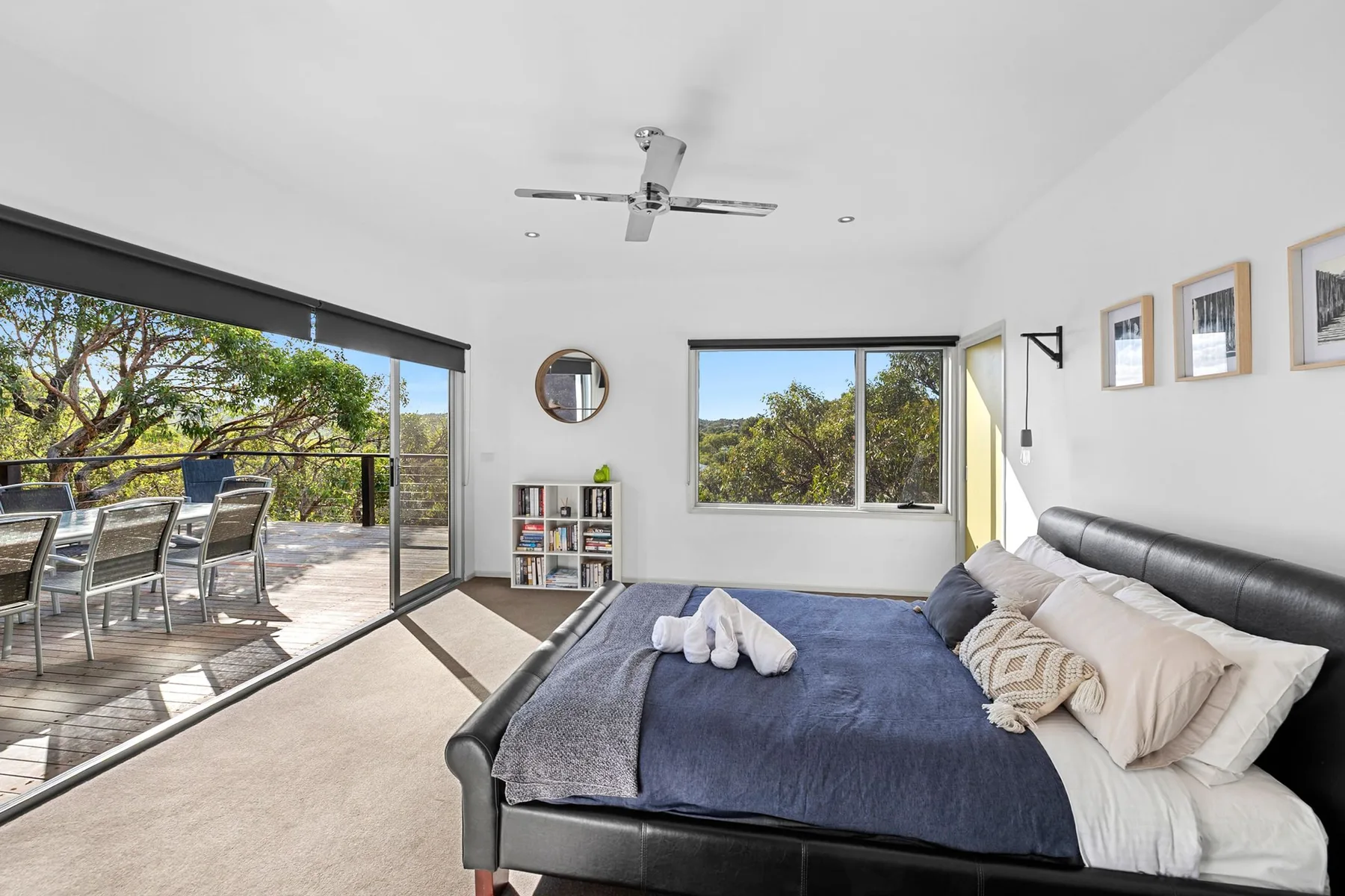 A bright bedroom opens onto a furnished balcony through wide sliding glass doors.