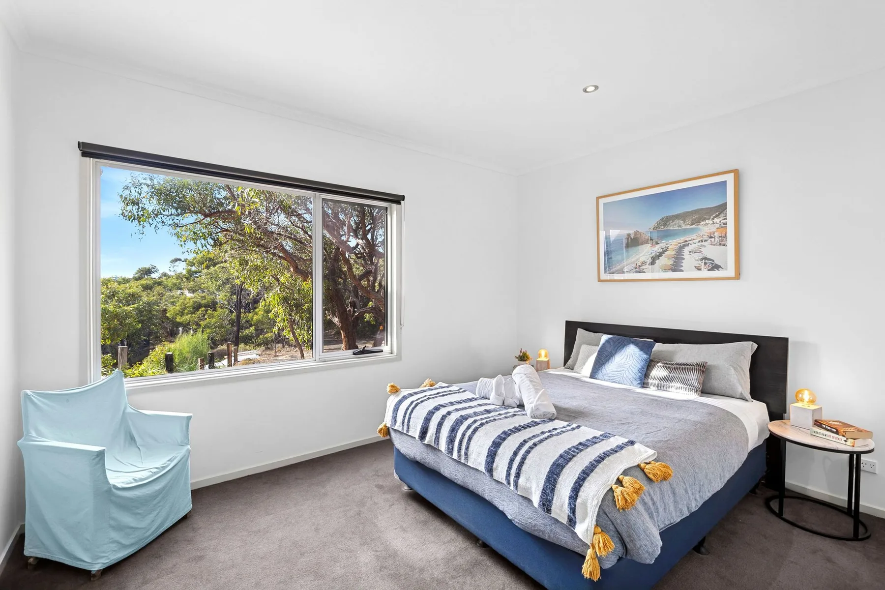 A bright bedroom with a bed and a large window overlooking trees.