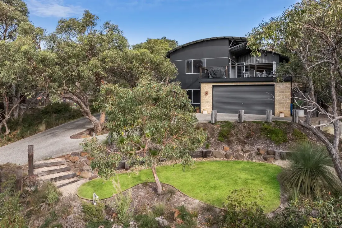 A modern house sits among trees above a small lawn and stone steps.