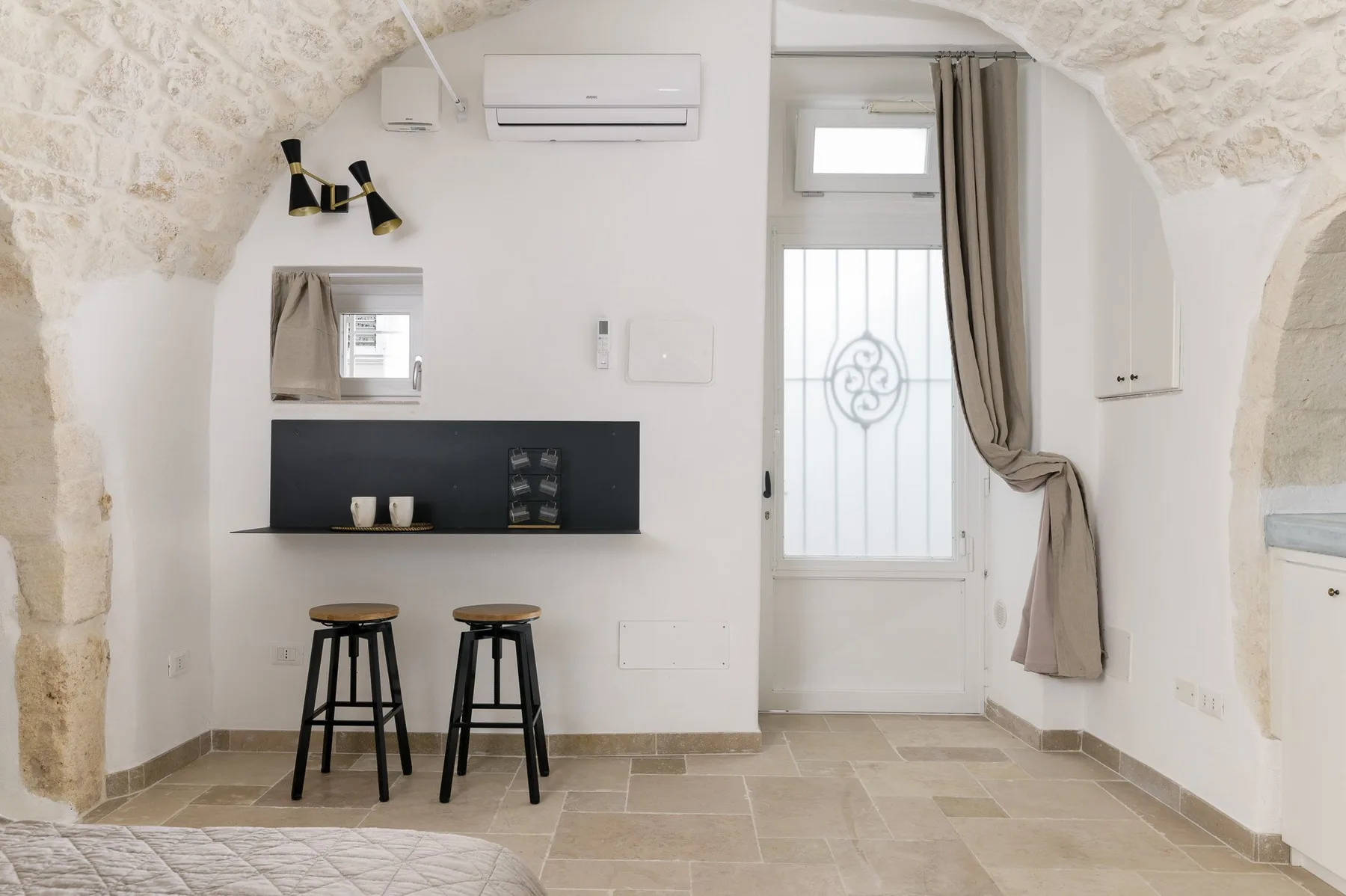 A bright room with a white door, a dark wall shelf, and two stools.