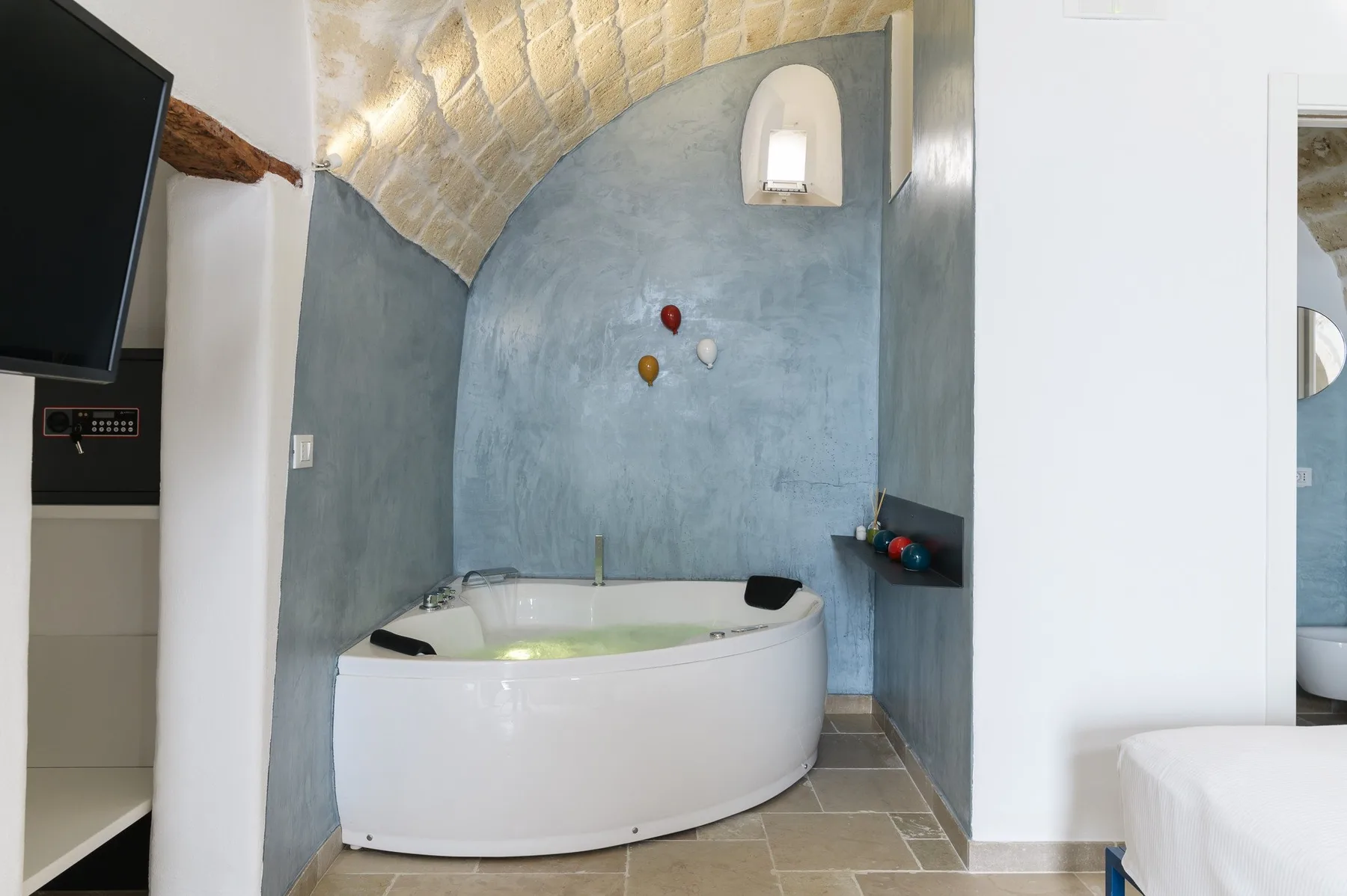 A curved bathtub sits beneath an arched ceiling in a tiled bathroom.