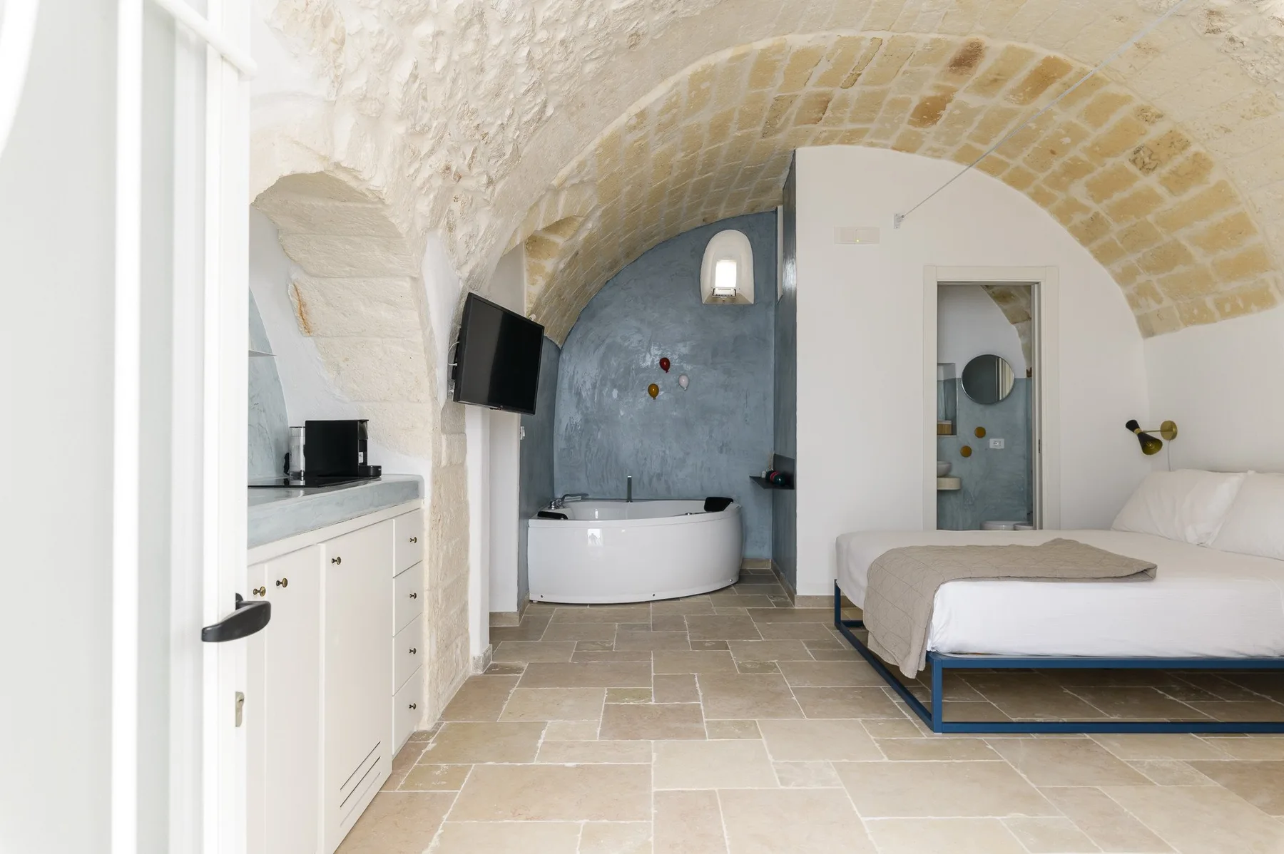 A bedroom with a bed, bathtub, and arched stone ceiling.