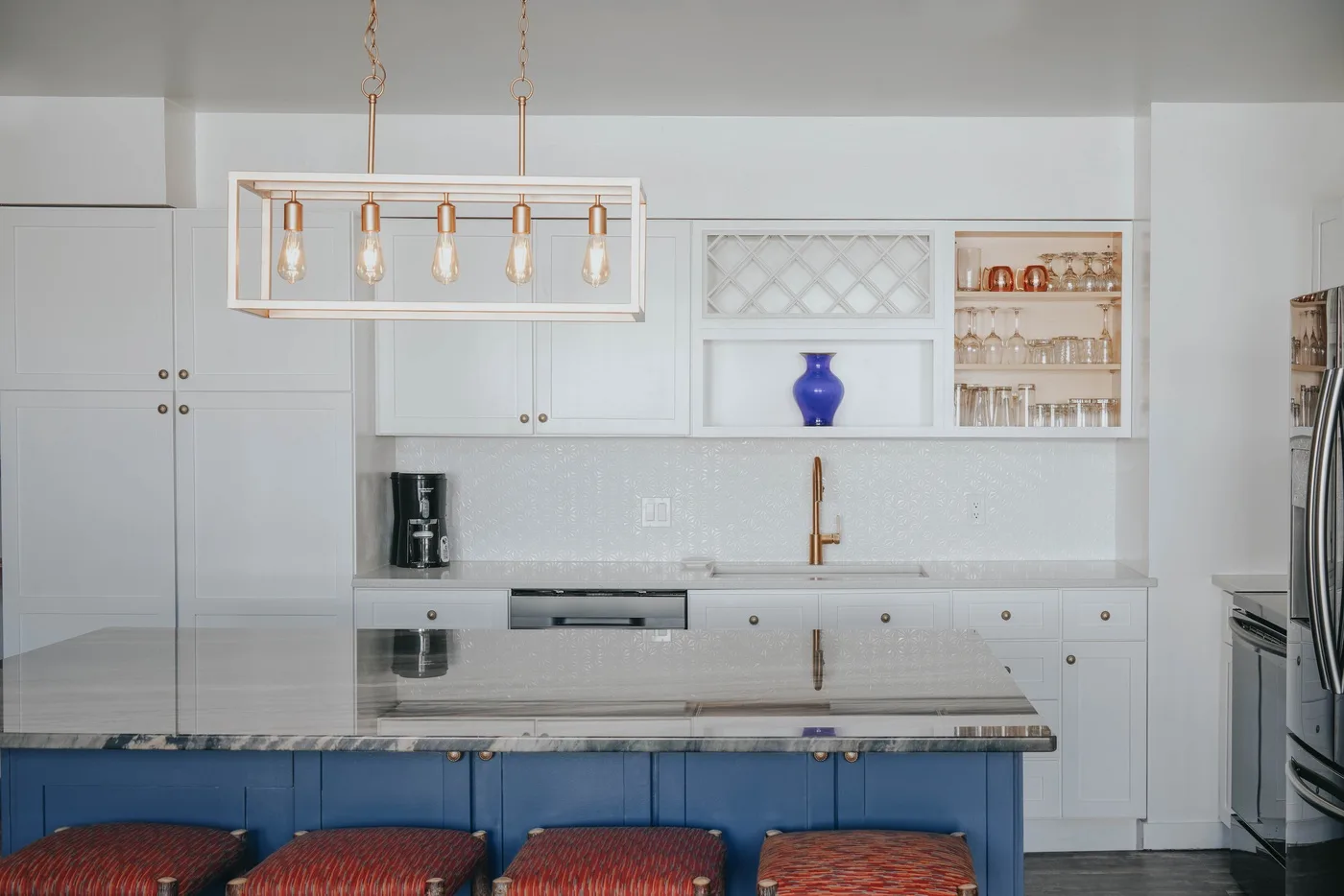 A bright kitchen with white cabinetry, a blue island, and hanging lights.