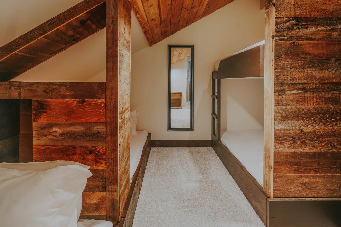 A narrow attic bedroom area with a bed beside a carpeted passage.