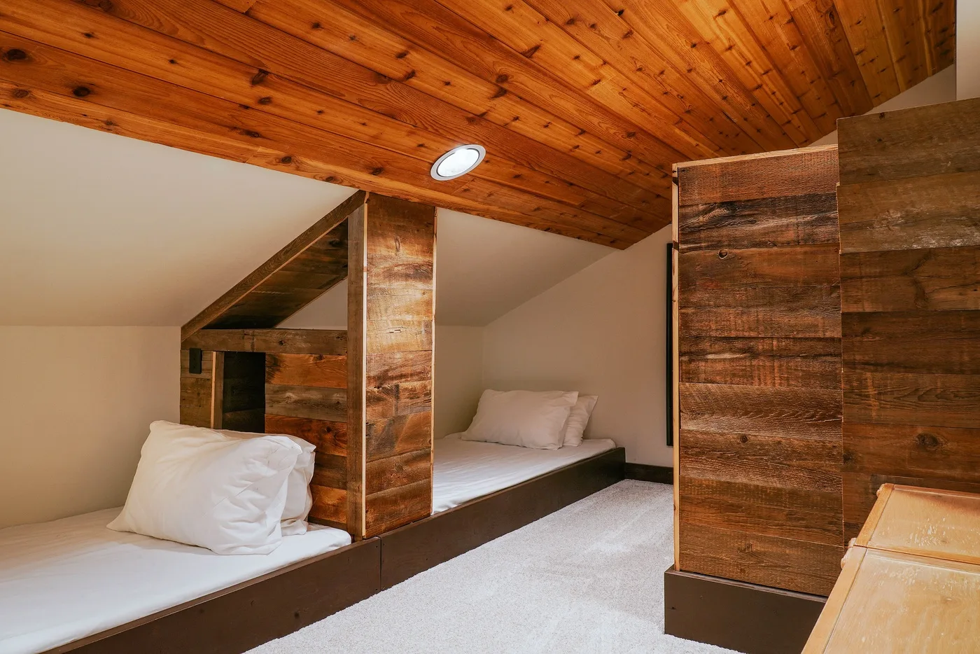 A bedroom with raised sleeping platforms beneath a sloped wooden ceiling.
