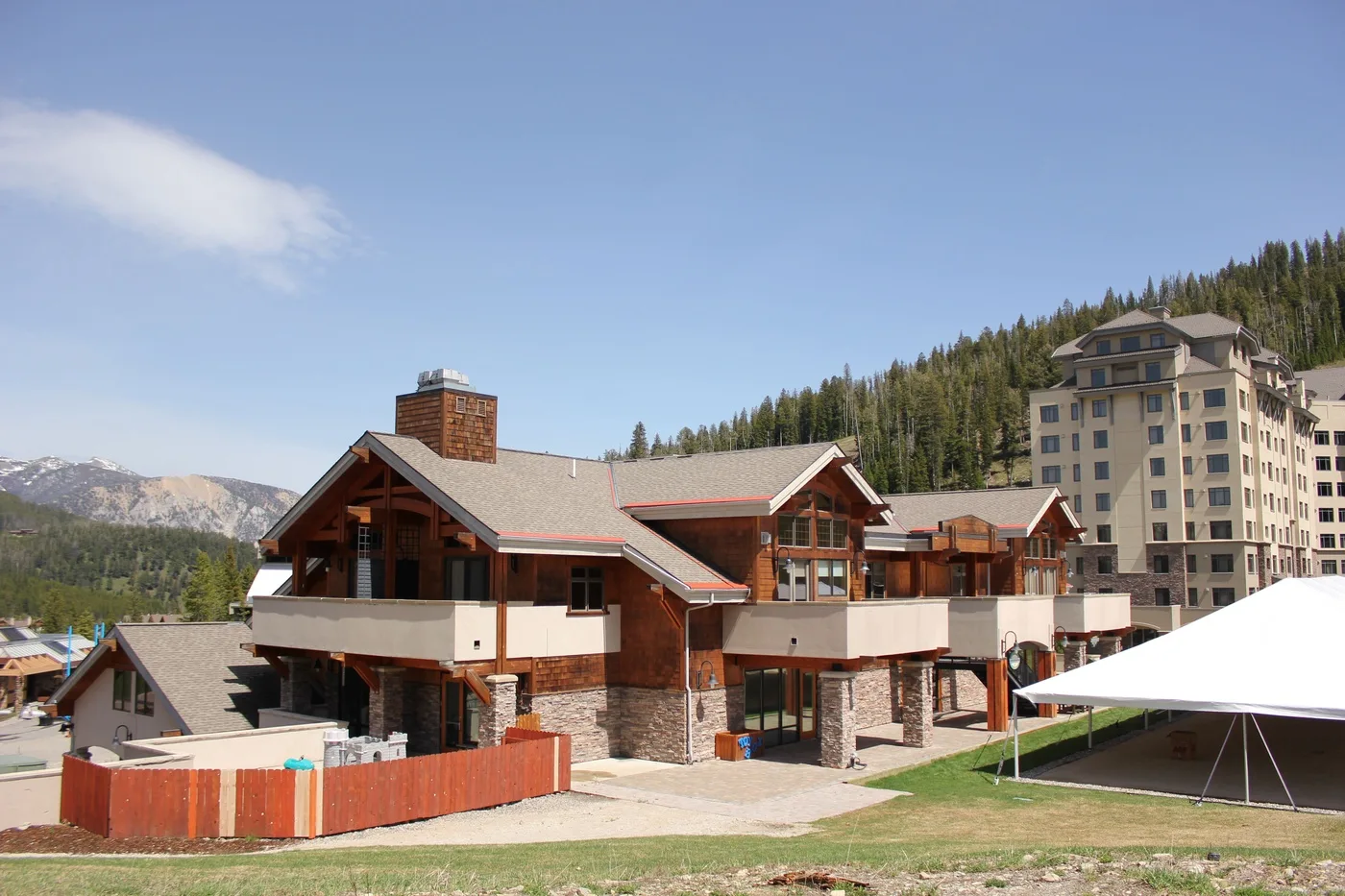 A large mountain lodge with timber details stands beside a grassy outdoor area.
