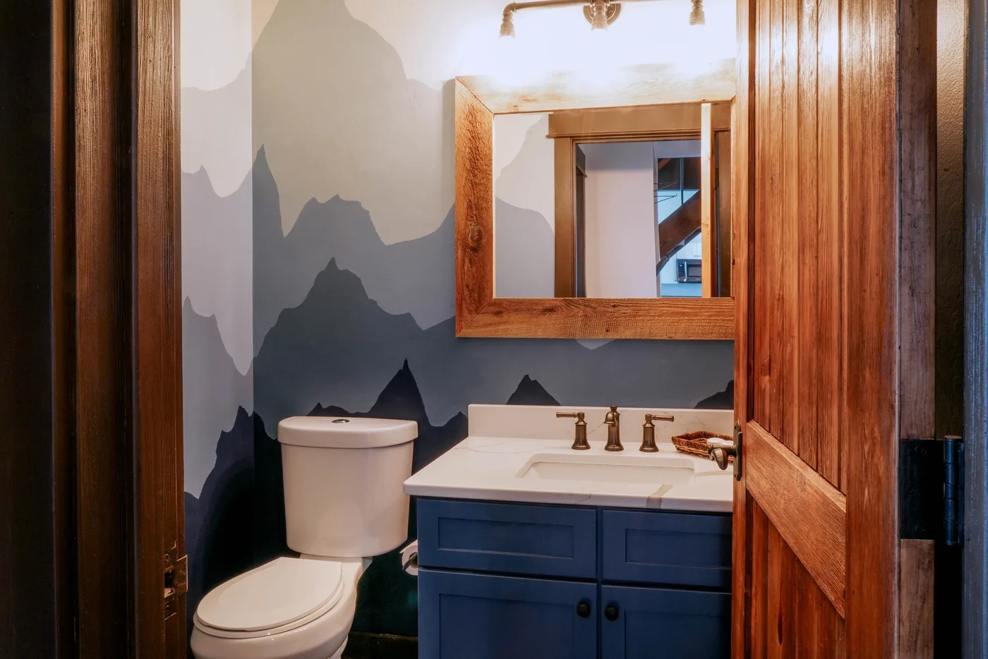 A bathroom with a toilet, vanity, and mountain-patterned wall.