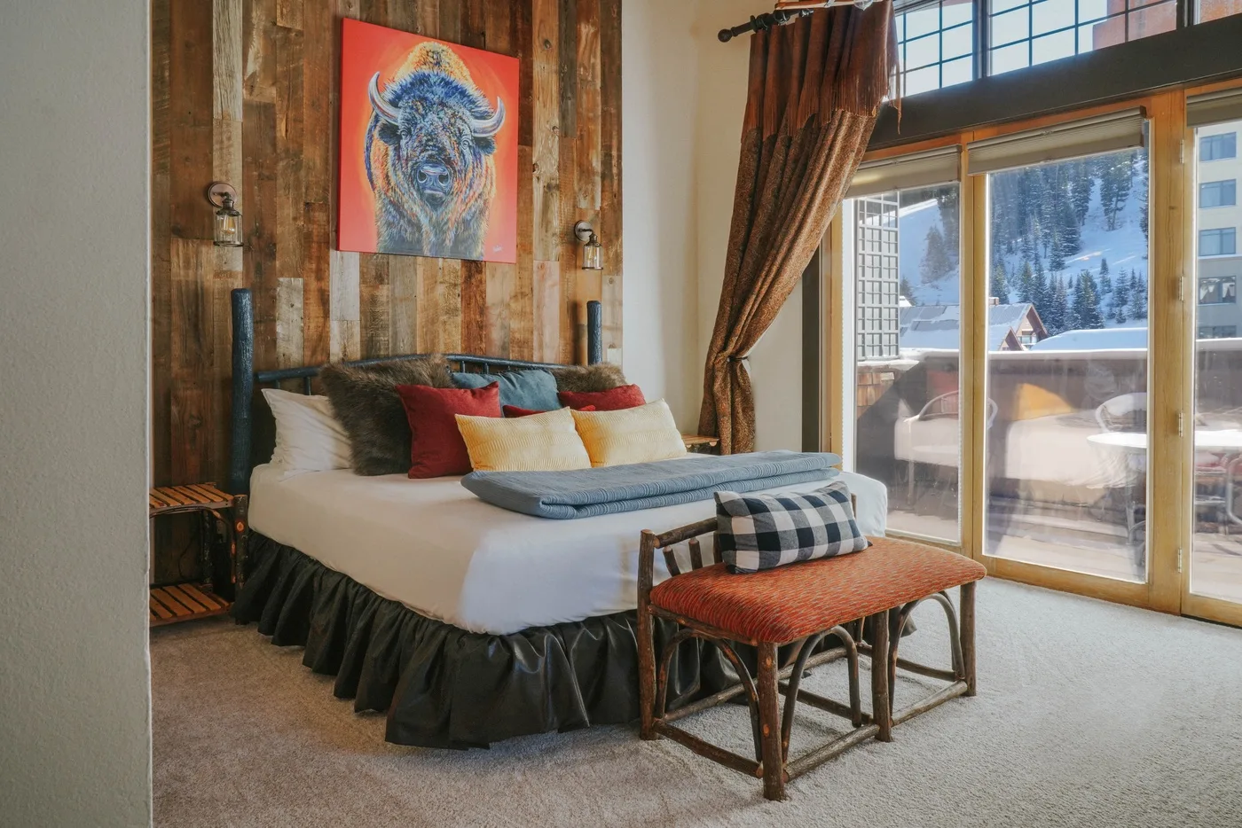 A bedroom with a bed and a large window overlooking a snowy landscape.