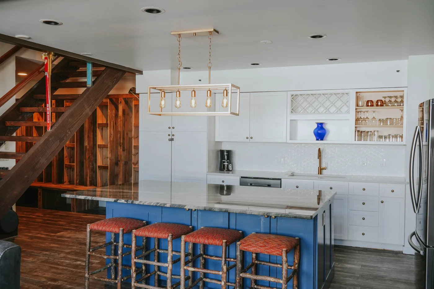 A bright kitchen with a blue island and wooden seating.