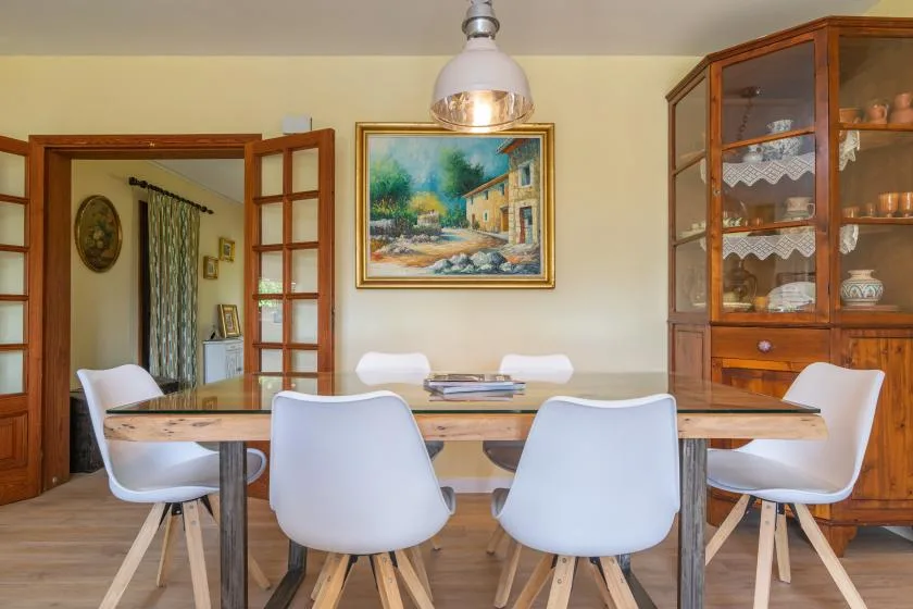 A dining area with a wooden table, white seating, and a glass-front cabinet.