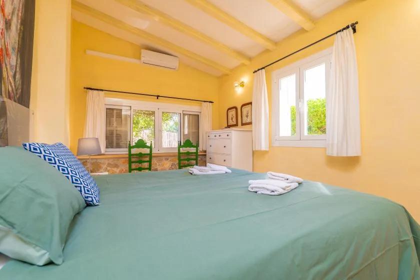 A bright bedroom with a large bed and windows dressed with white curtains.