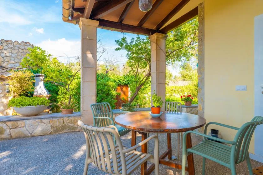 A covered outdoor patio with a round table and green seating overlooks a garden.