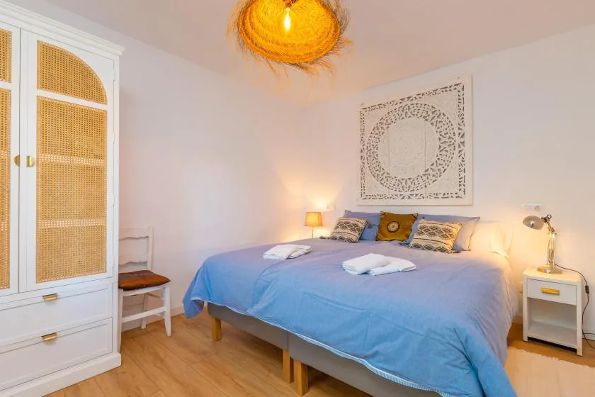 A bedroom with a blue-covered bed, bedside tables, and a woven ceiling light.