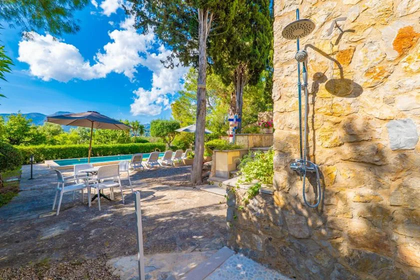 An outdoor patio with seating and an open-air shower beside a stone wall.