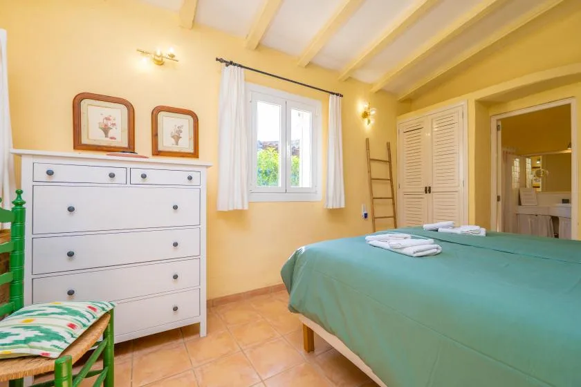 A bedroom with a green-covered bed beside a window and white dresser.