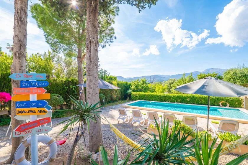 An outdoor swimming pool is surrounded by lounge seating, trees, and greenery.