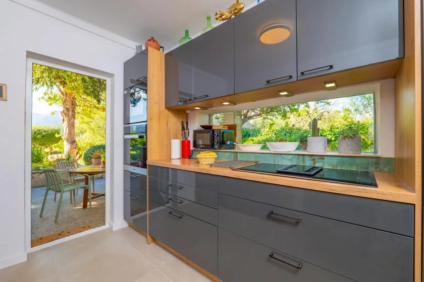 A modern kitchen with dark cabinets and a long window above the counter.
