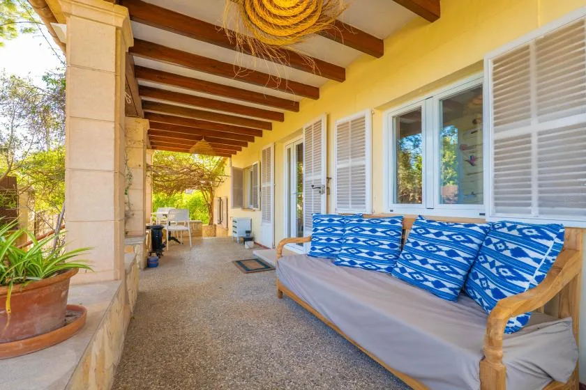 A covered porch has cushioned seating beside windows with open shutters.