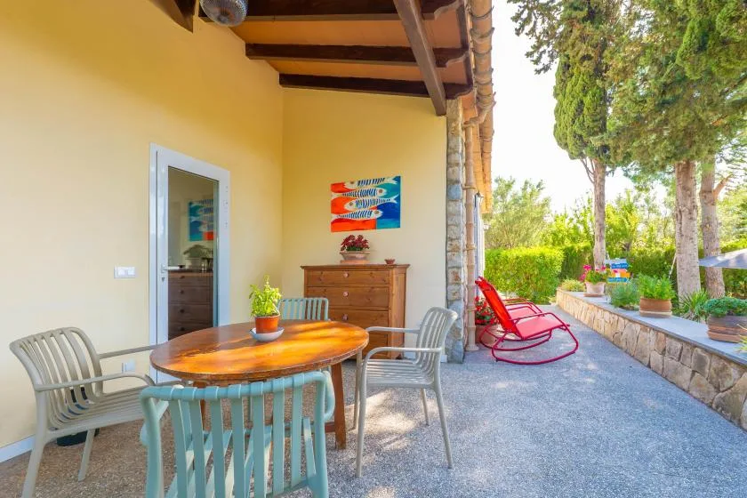 A covered patio has a dining table and chairs beside a garden path.