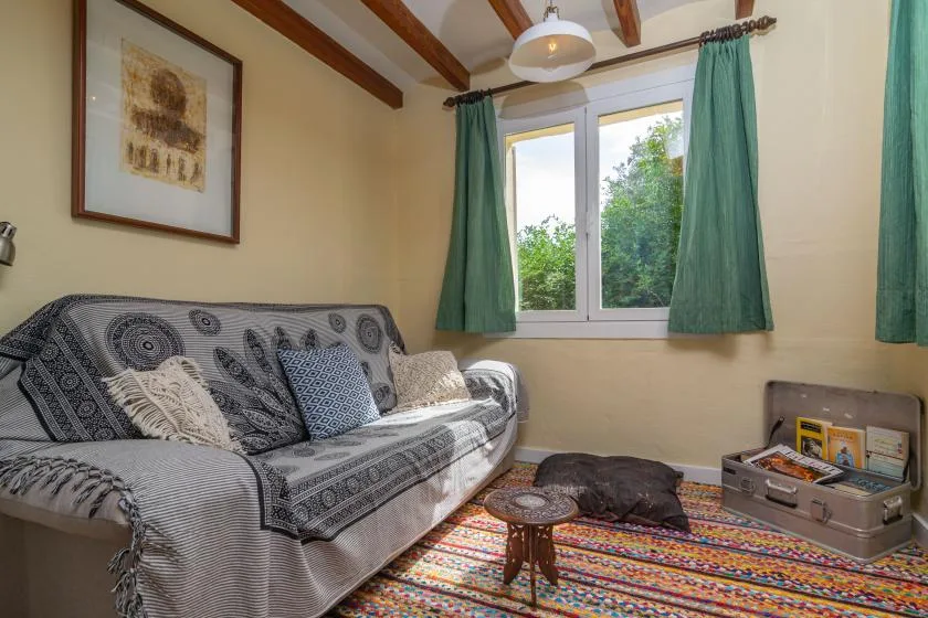 A living room with patterned seating, a colorful rug, and a window overlooking greenery.