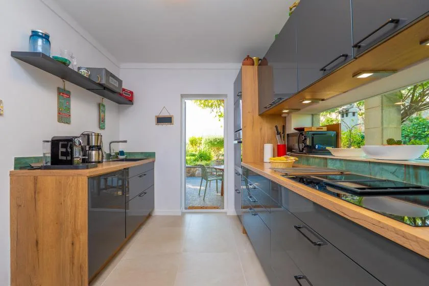 A modern kitchen with dark cabinets and a glass door opening onto greenery.