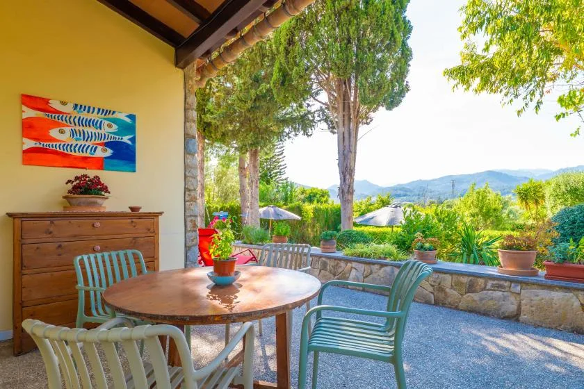 An outdoor patio with a round table and chairs overlooks a green landscape.