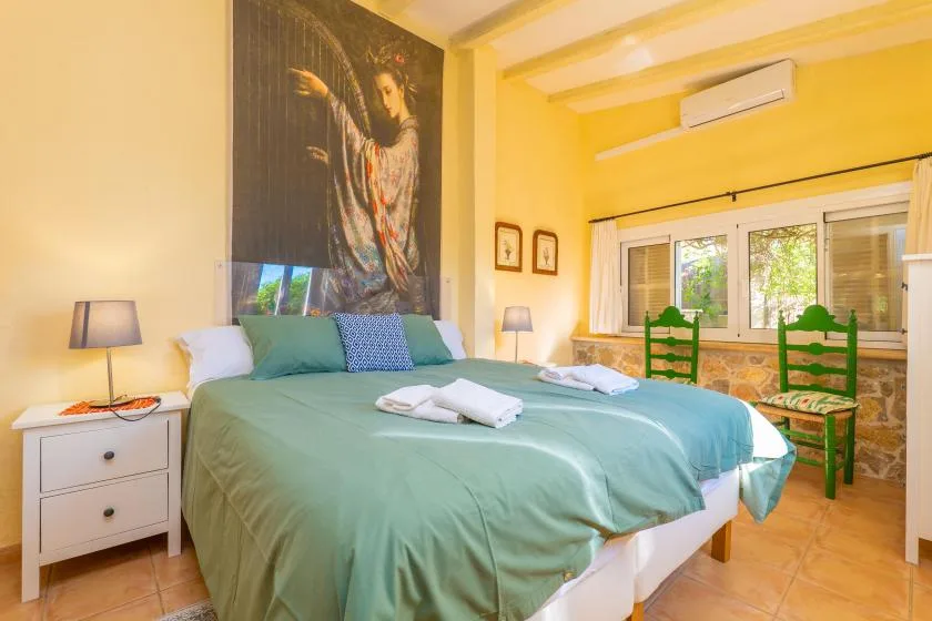 A bedroom with a bed dressed in green bedding and a large wall painting.
