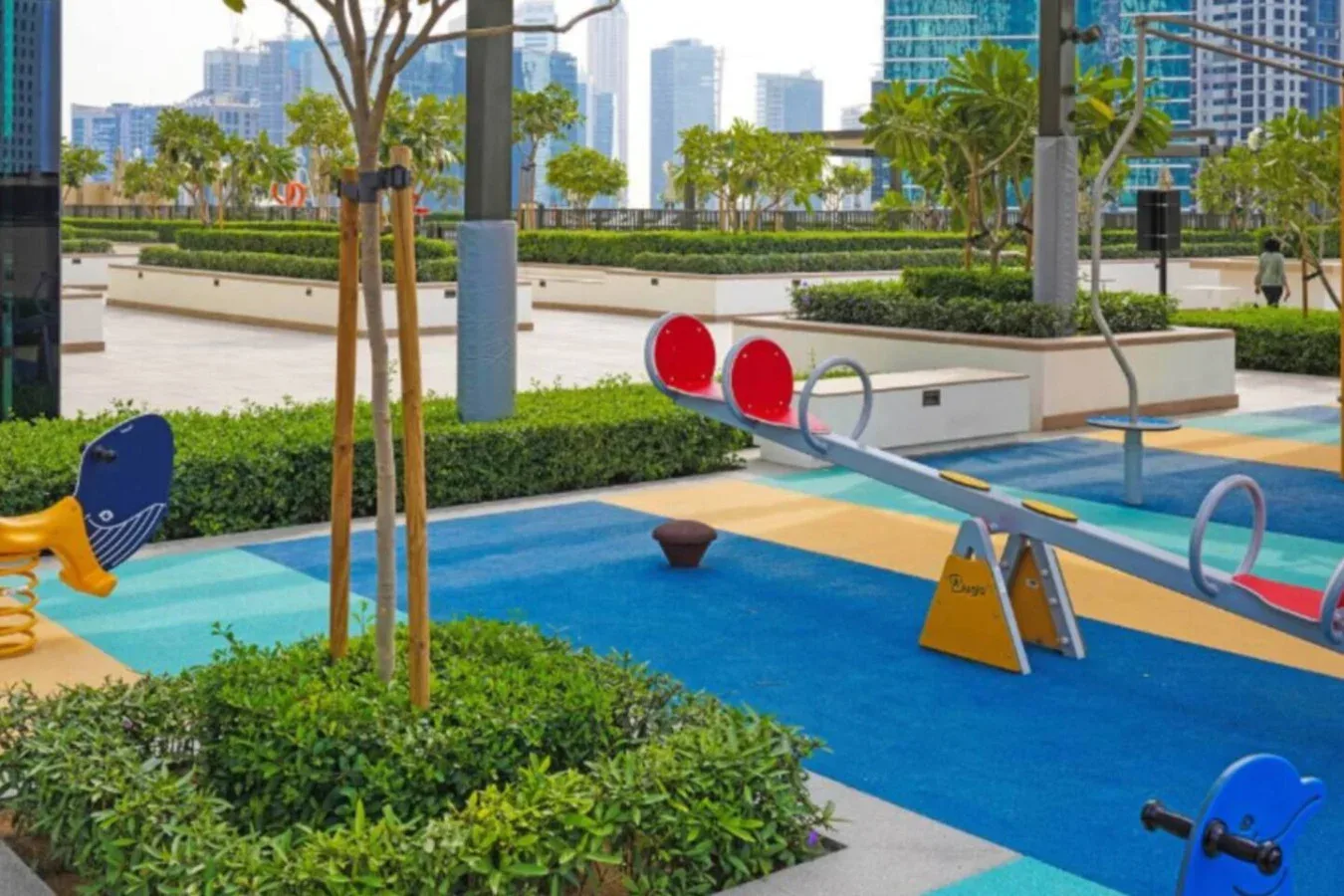 Un parque infantil al aire libre con juegos azules y amarillos junto a zonas verdes.