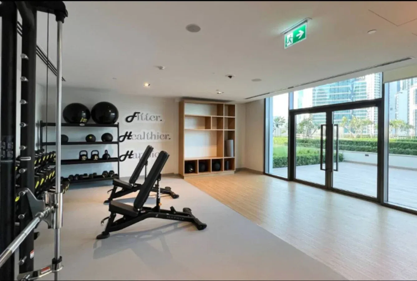Una sala de ejercicios con equipo de entrenamiento, estantes y grandes ventanas.