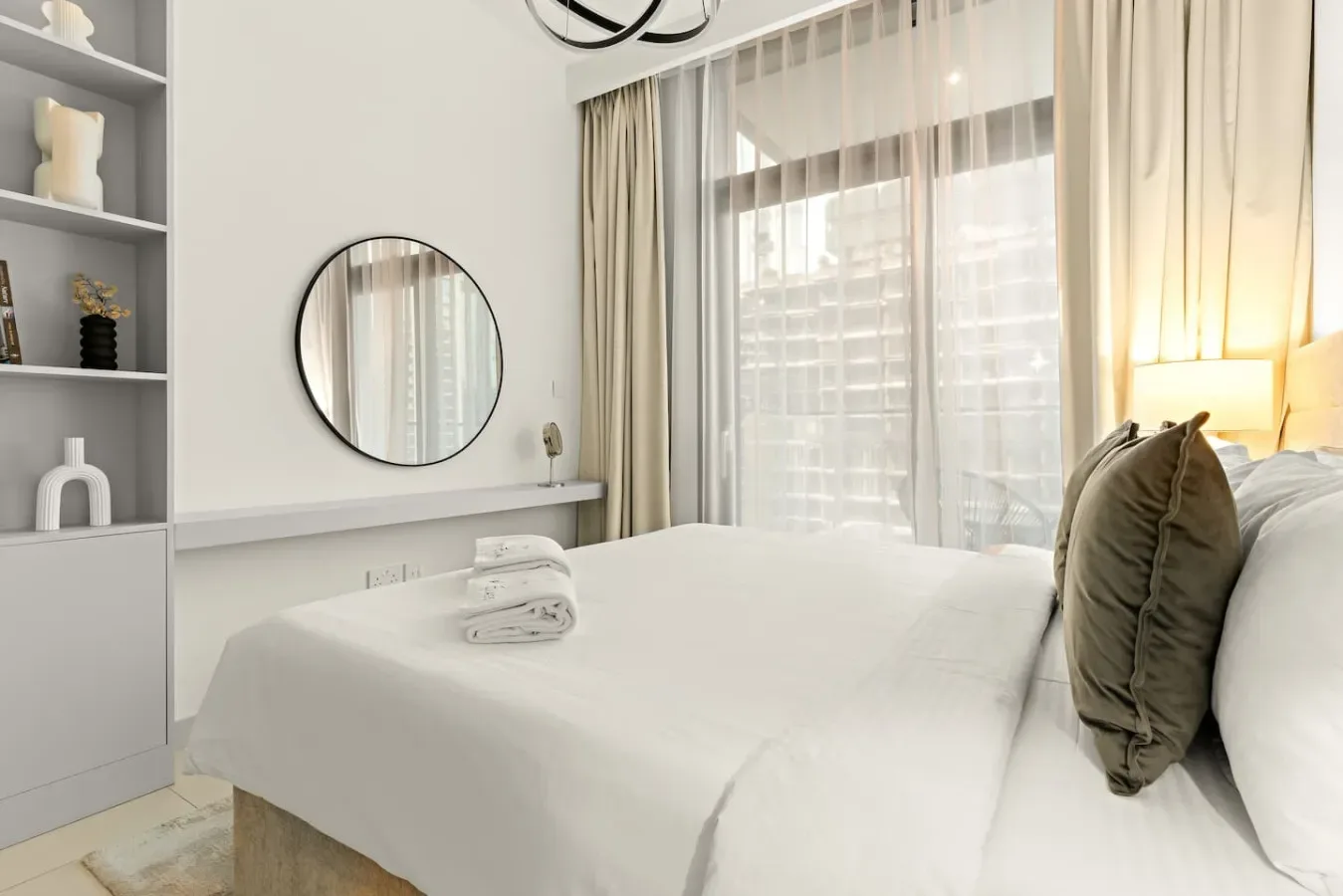Un dormitorio luminoso con una cama bien hecha junto a una gran ventana con cortinas.